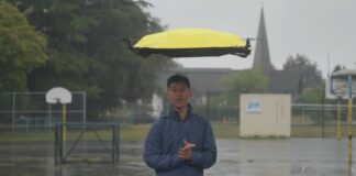 John Xu standing in heavy rain beneath his autonomous flying drone umbrella
