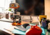 MicroDuck biped robot standing on a desk beside a computer and game controller