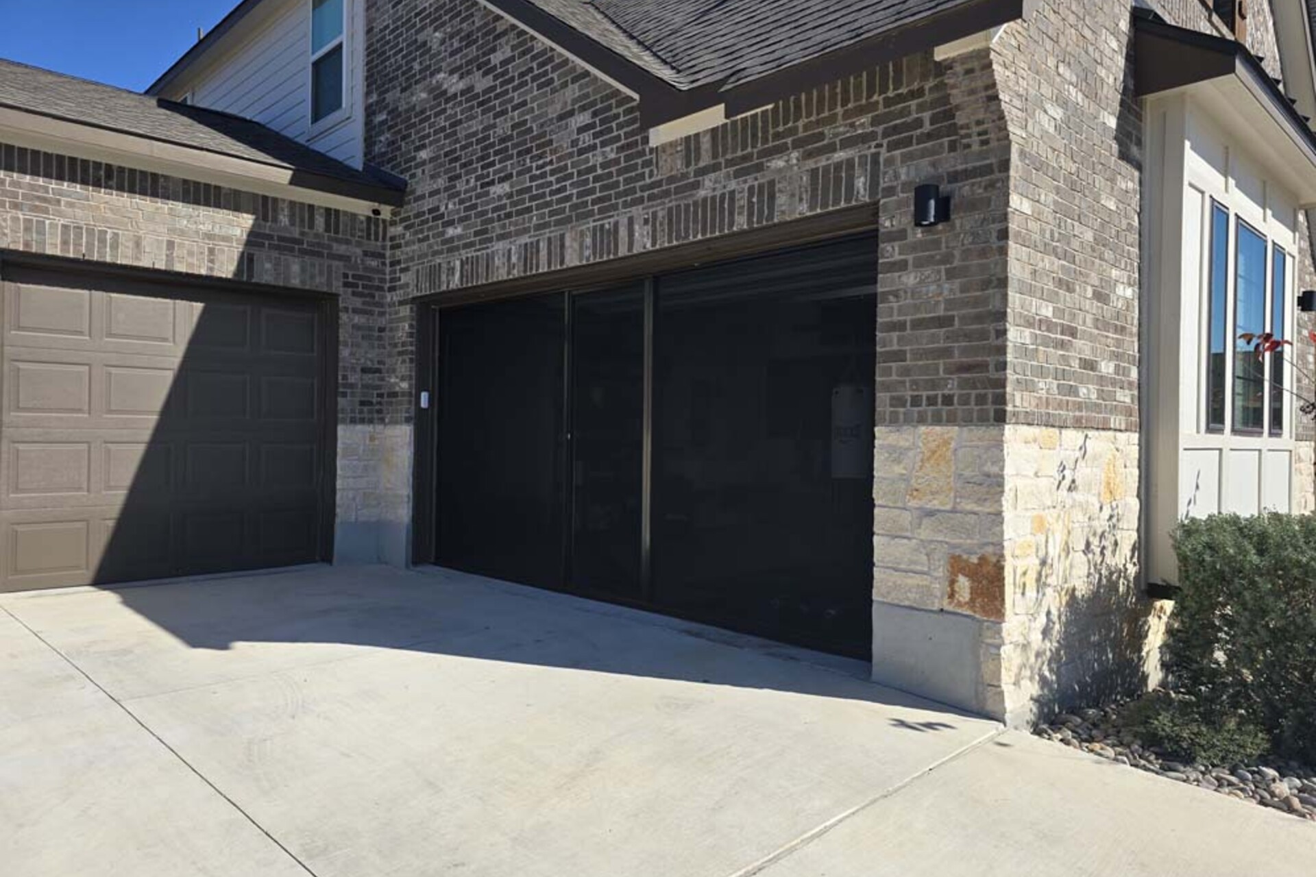 Lifestyle garage-door screen with a black frame installed on a brick home