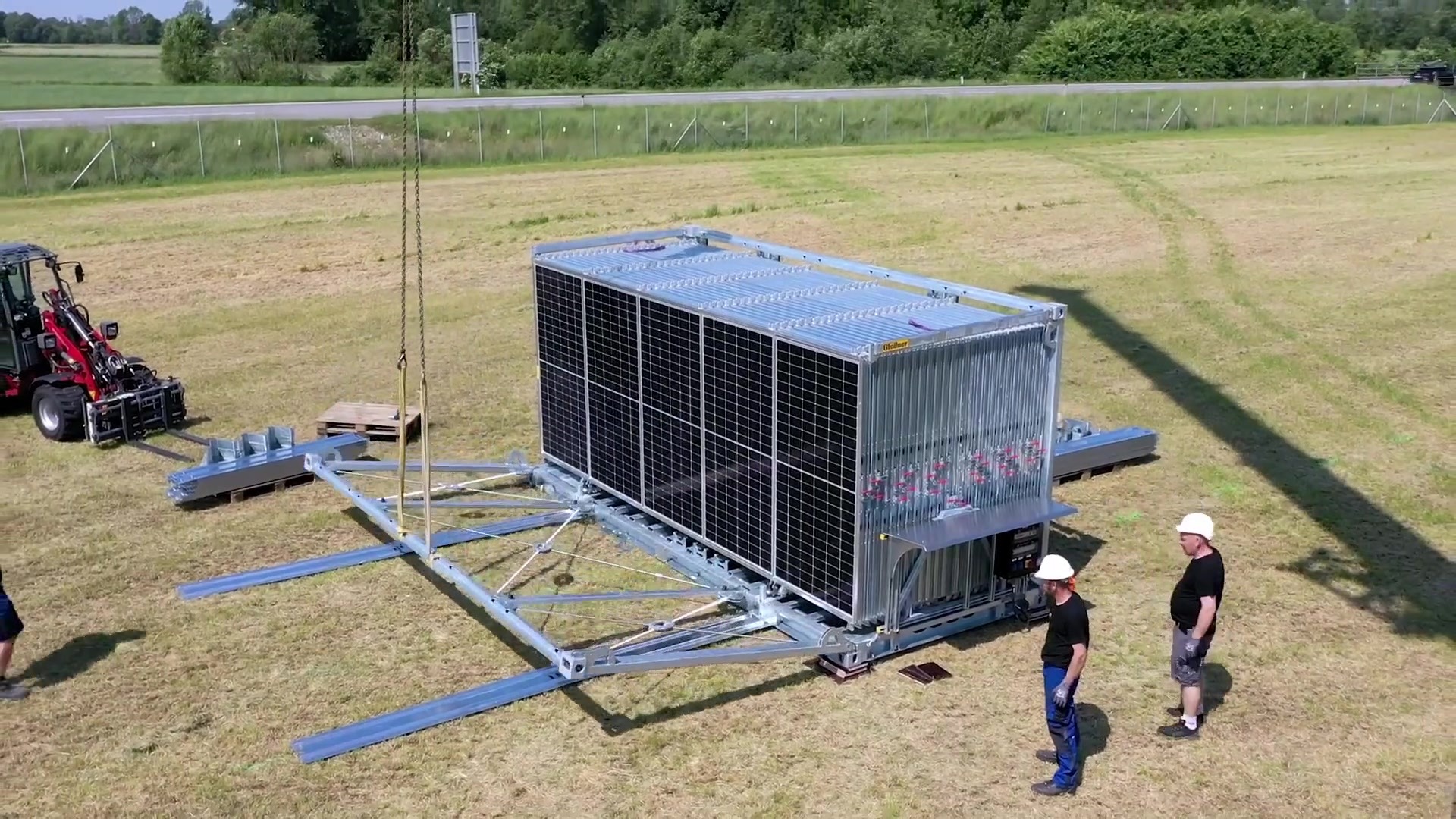 Workers installing galvanized steel rails beside a folded Solarcontainer
