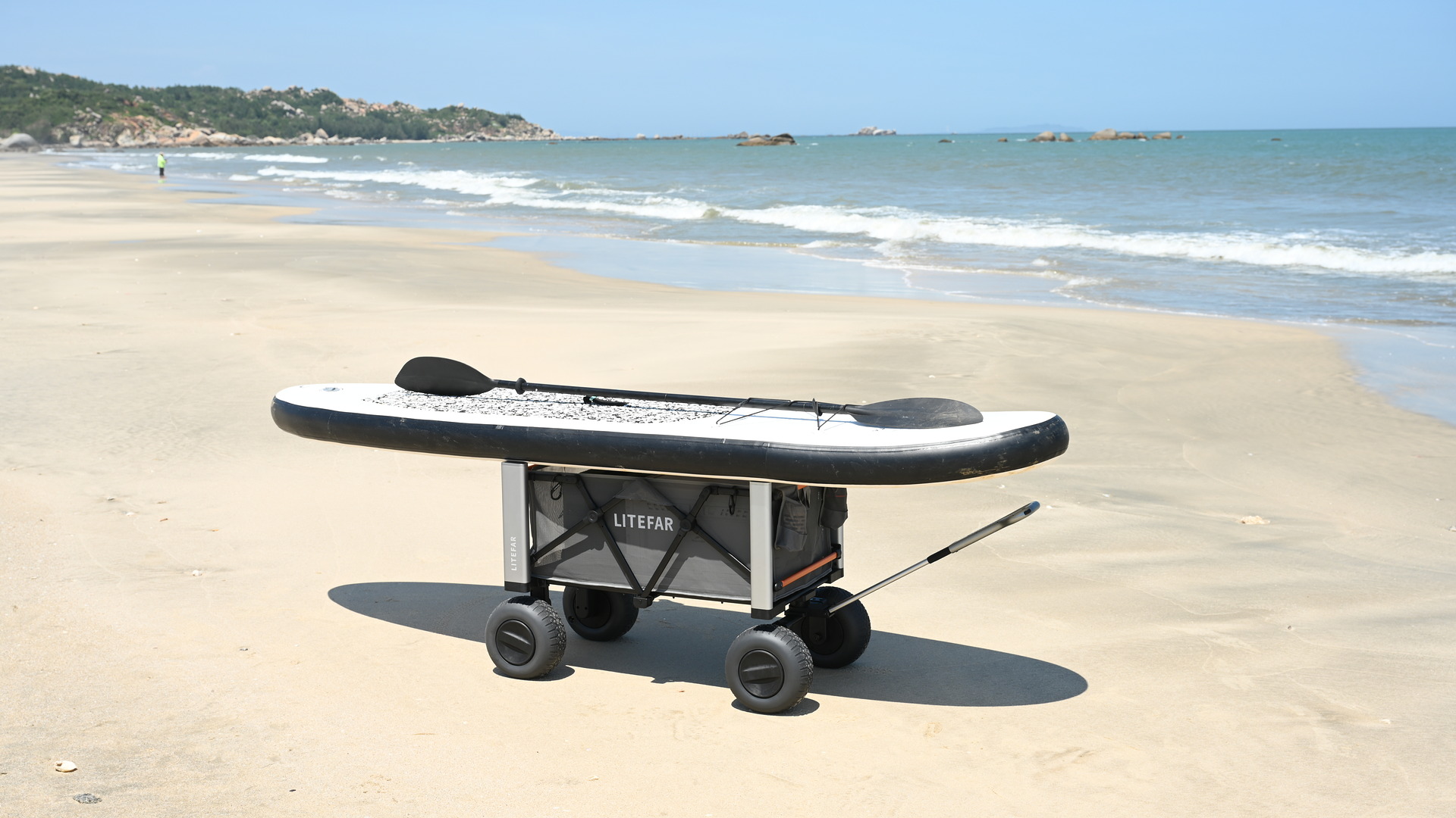 Paddleboard and paddle secured on top of the LITEFAR B1 electric beach wagon on sand