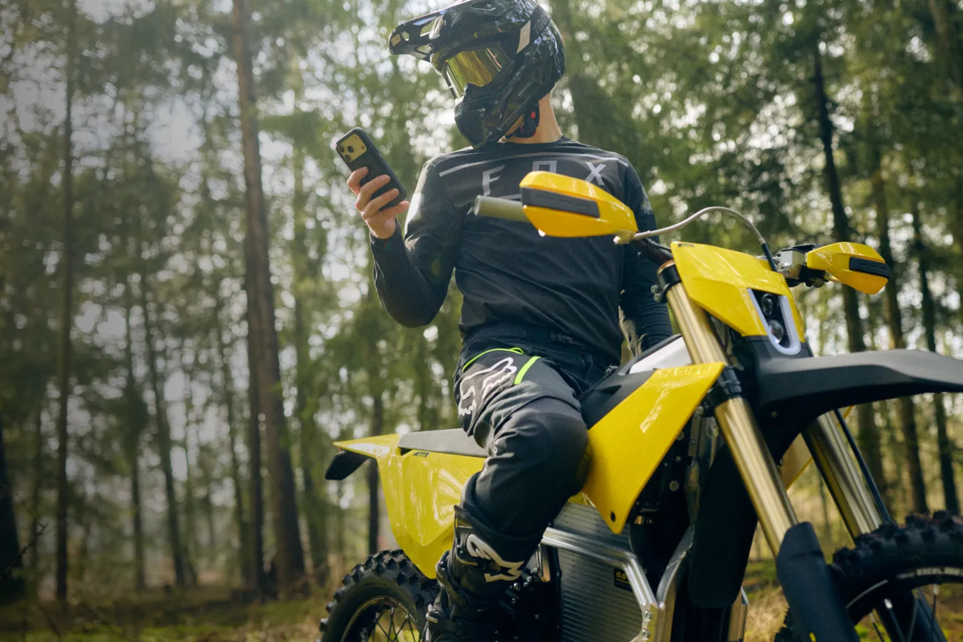 Radian EXR rider using a smartphone beside the electric motorcycle in a forest