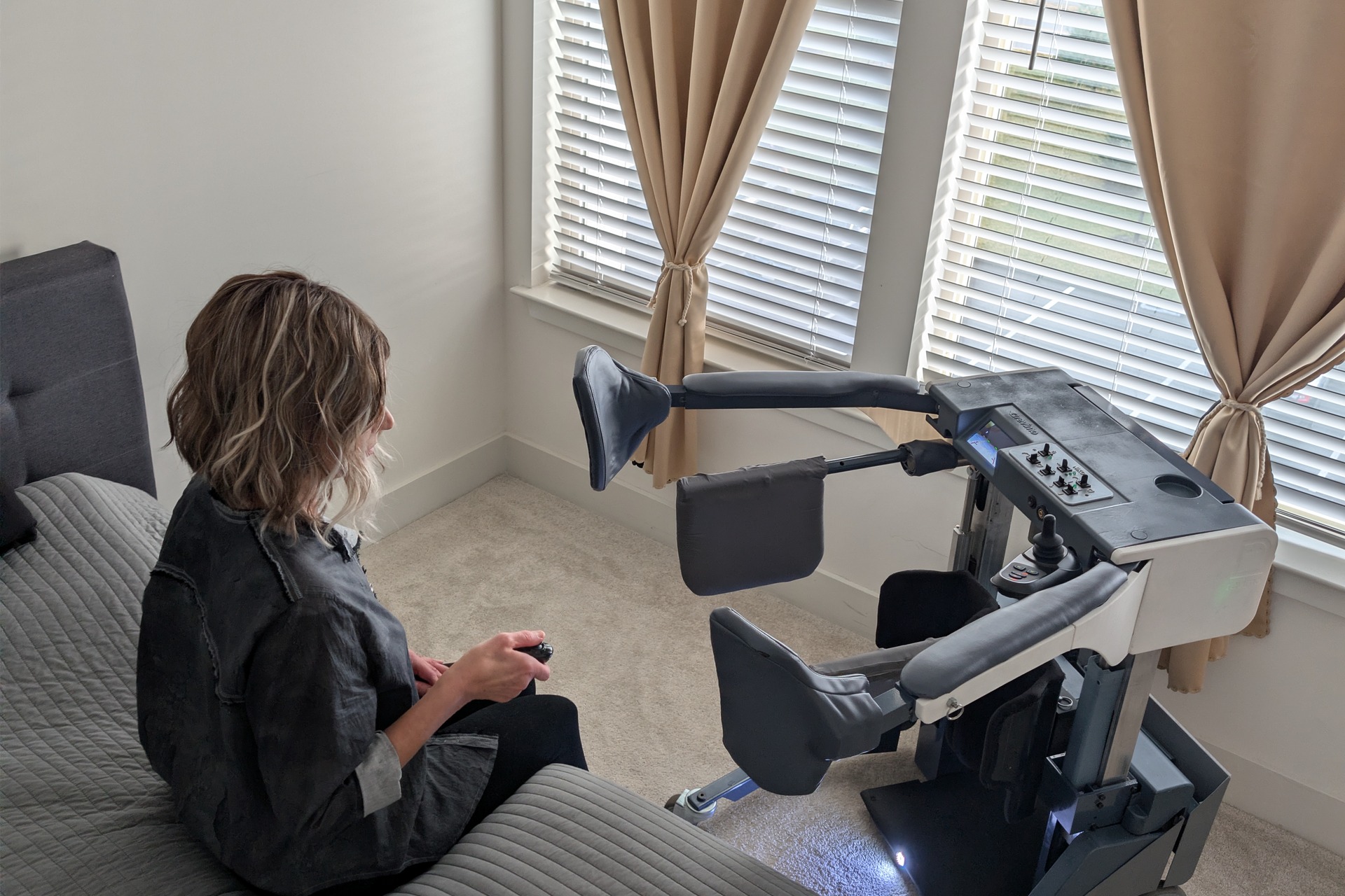Woman operating the REVIMO Niko beside a bed using its wireless controller