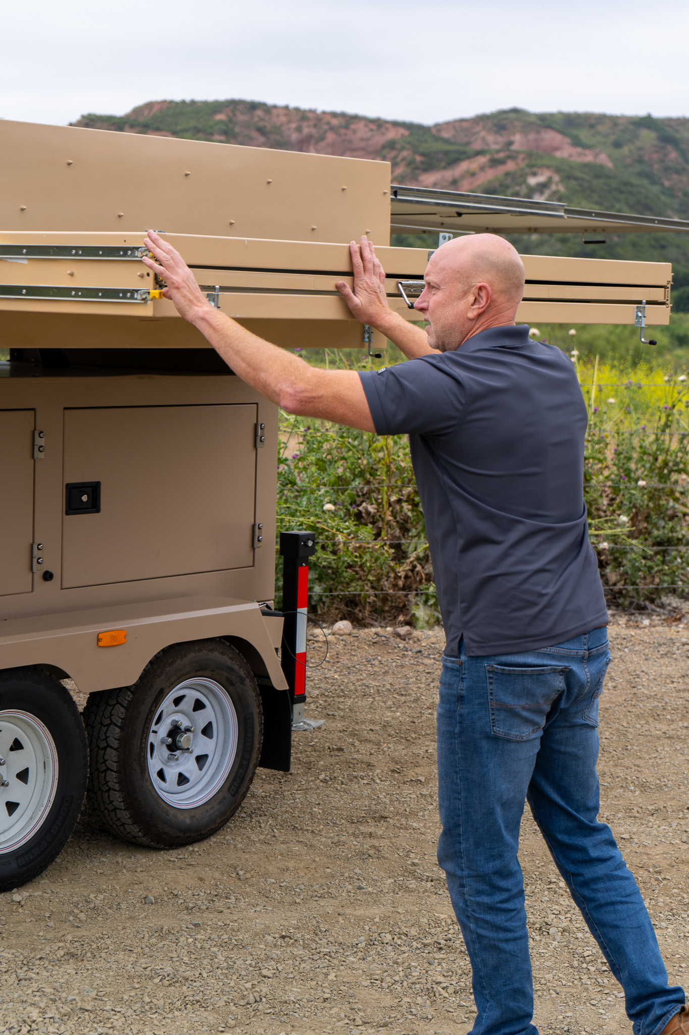 Operator beginning to deploy the folded solar-panel sections on a 123-STG-4 trailer
