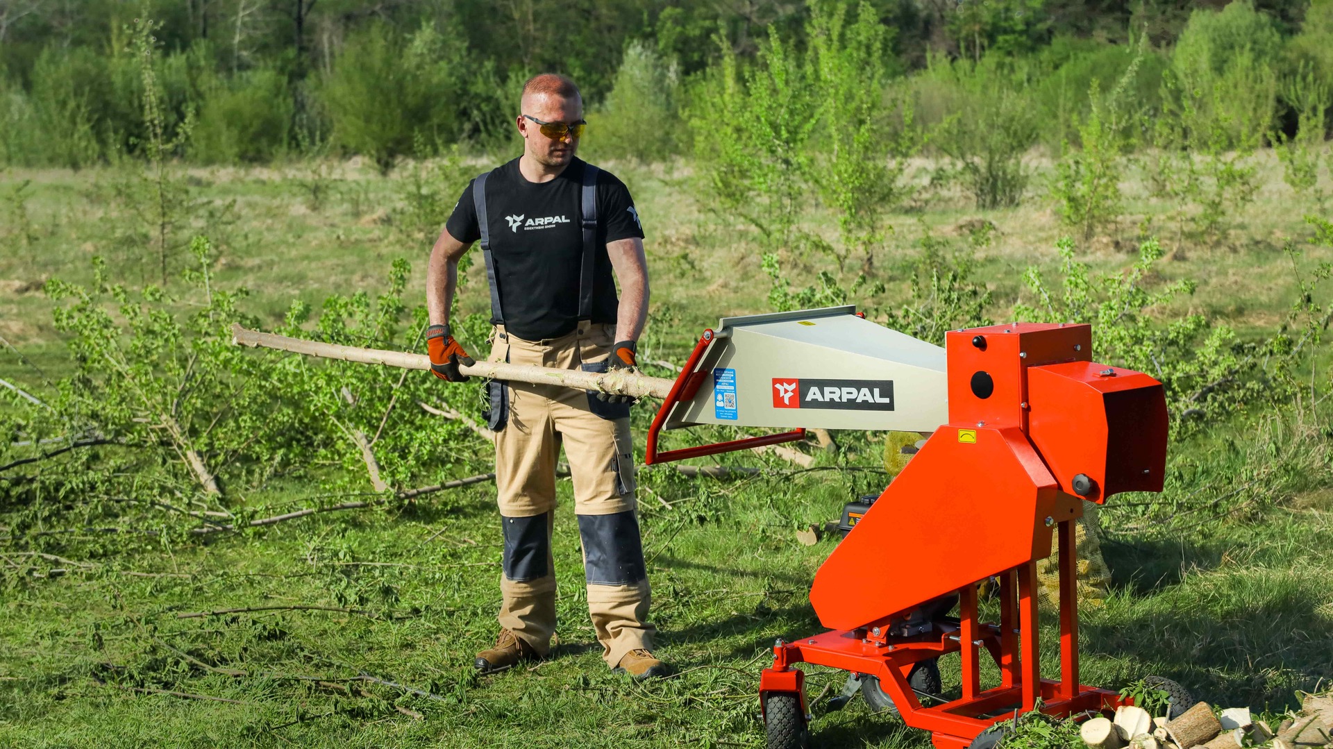 Operator holding branches beside the red ARPAL AM-80BD petrol wood chipper
