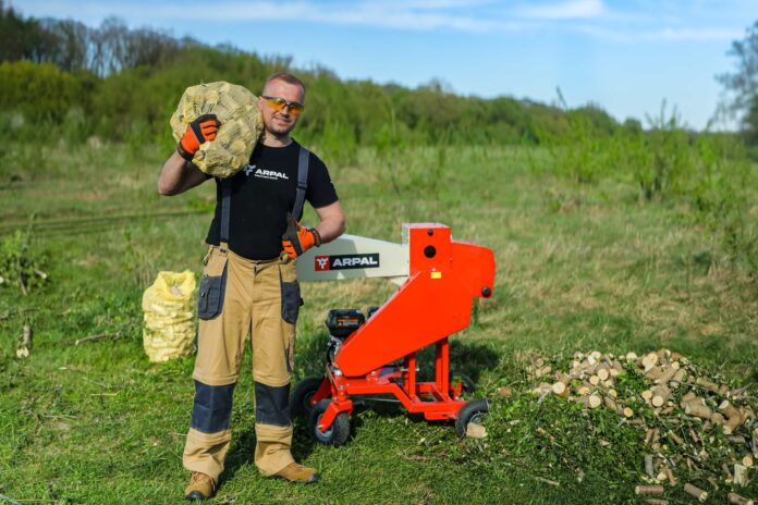 Operator standing beside the red ARPAL Classic AM-80BD wood chipper and bags of cut wood