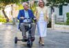 Older man riding an ATTO Sport mobility scooter beside a woman on a paved street