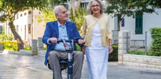 Older man riding an ATTO Sport mobility scooter beside a woman on a paved street