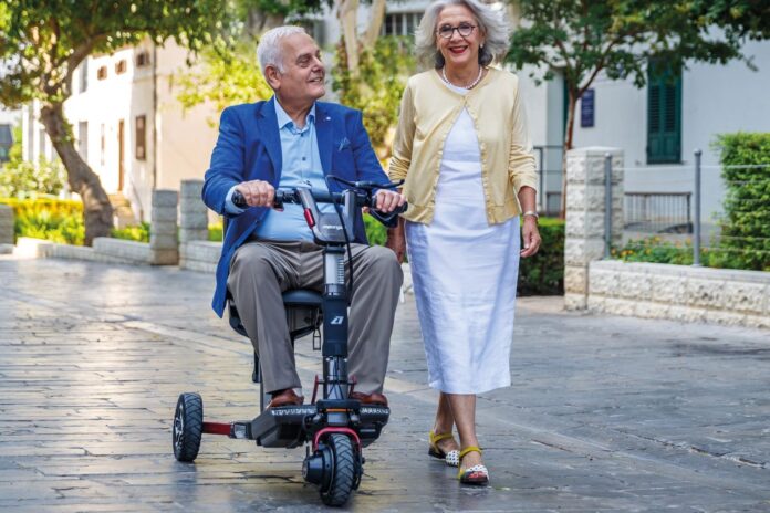 Older man riding an ATTO Sport mobility scooter beside a woman on a paved street