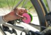 A cyclist holding the Green Disc+ applicator against a bicycle chain while turning the crank