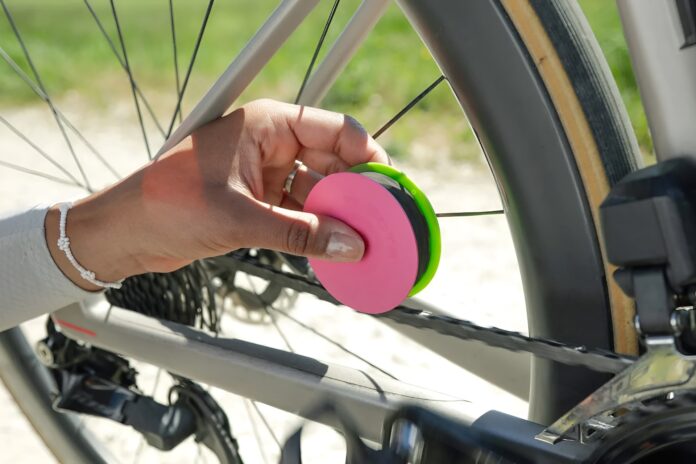 A cyclist holding the Green Disc+ applicator against a bicycle chain while turning the crank