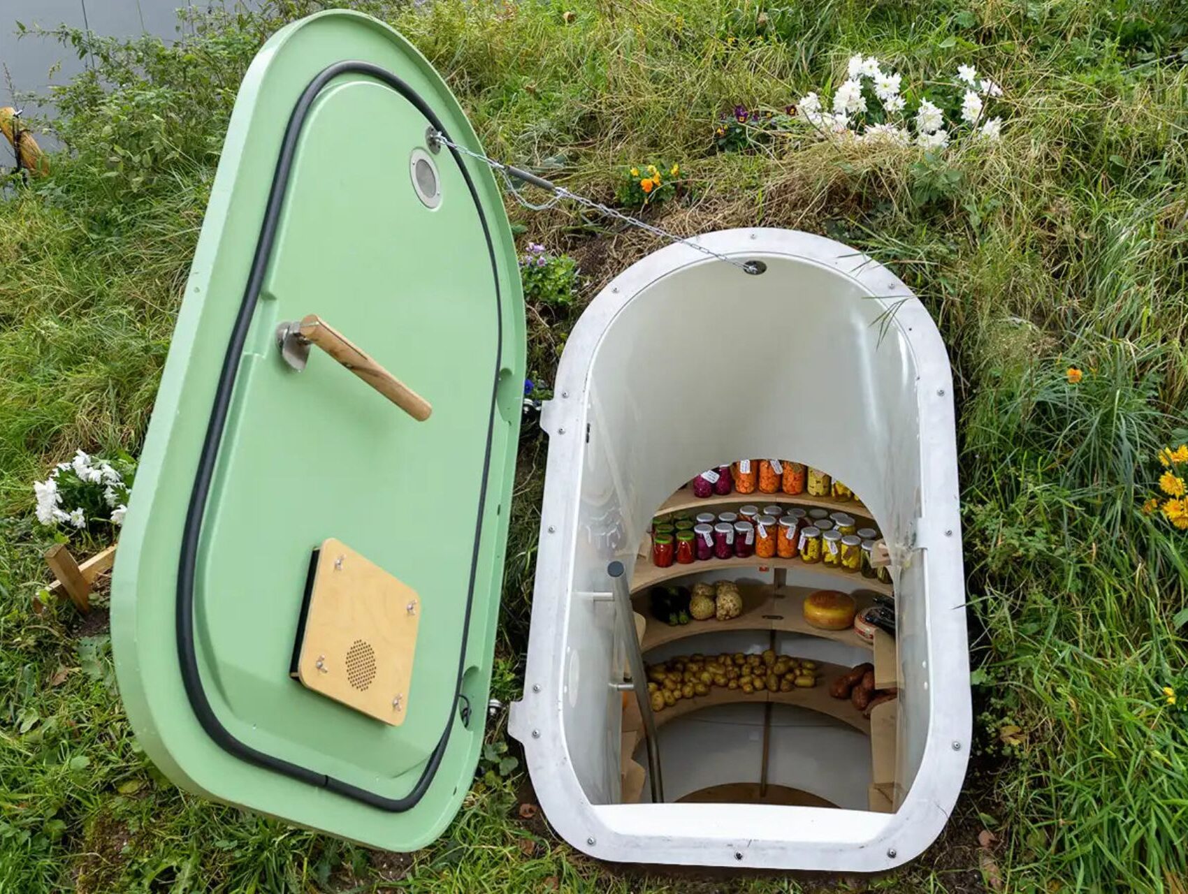 Green Groundfridge entrance surrounded by flowers and plants in a garden