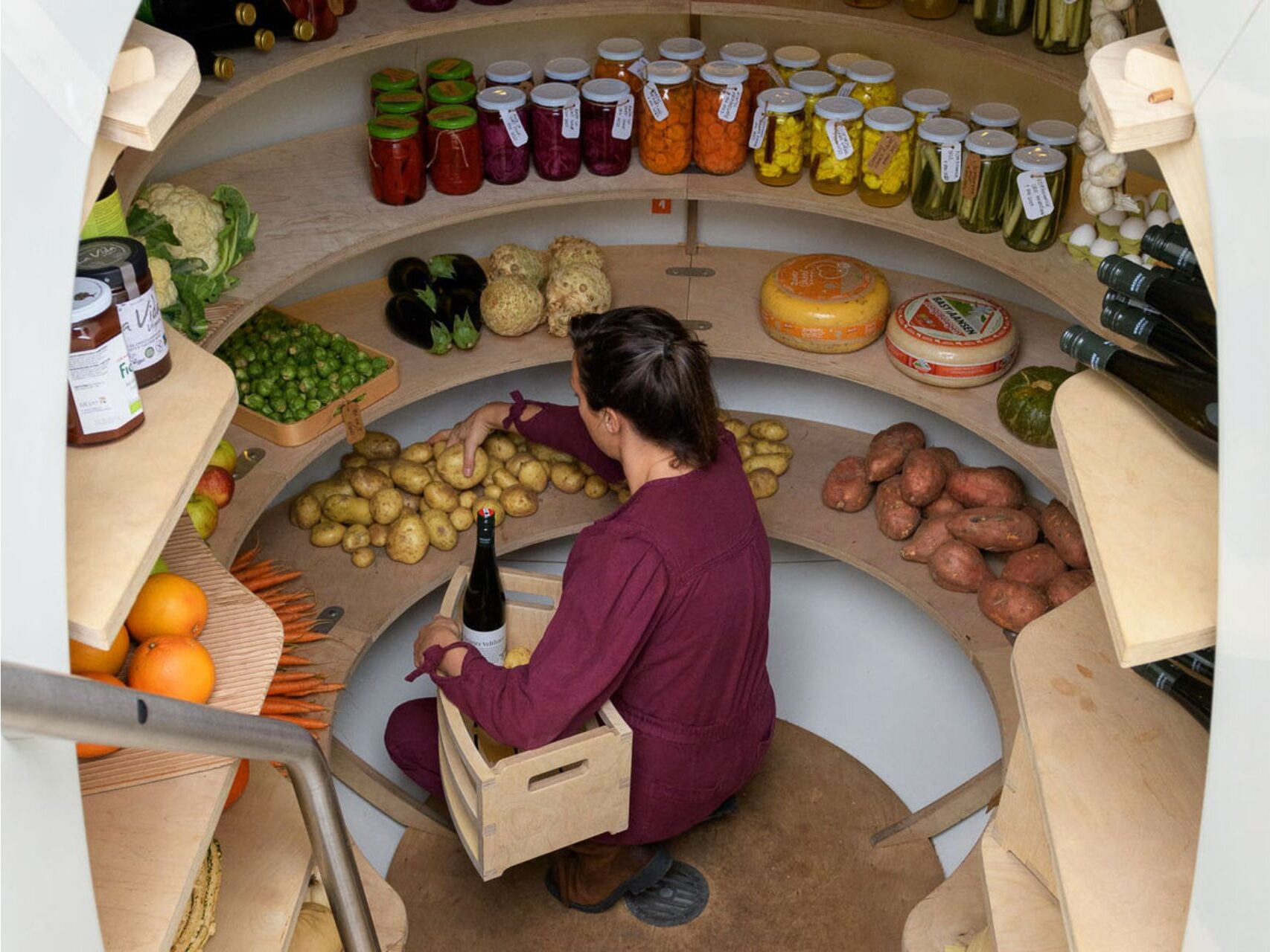 Woman arranging potatoes inside a Groundfridge stocked with vegetables, preserves, cheese and wine