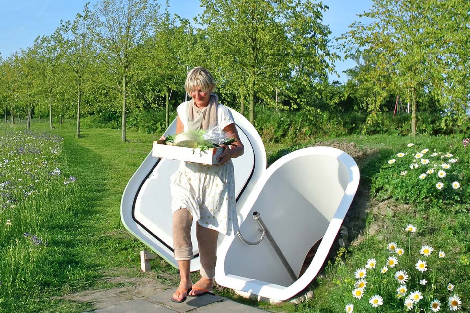 Woman carrying a crate of fresh produce out of a Groundfridge in a garden
