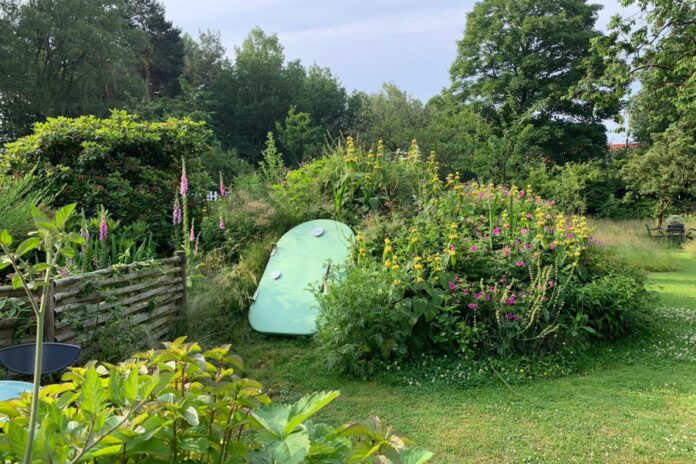 Green Groundfridge entrance surrounded by flowers and plants in a landscaped garden