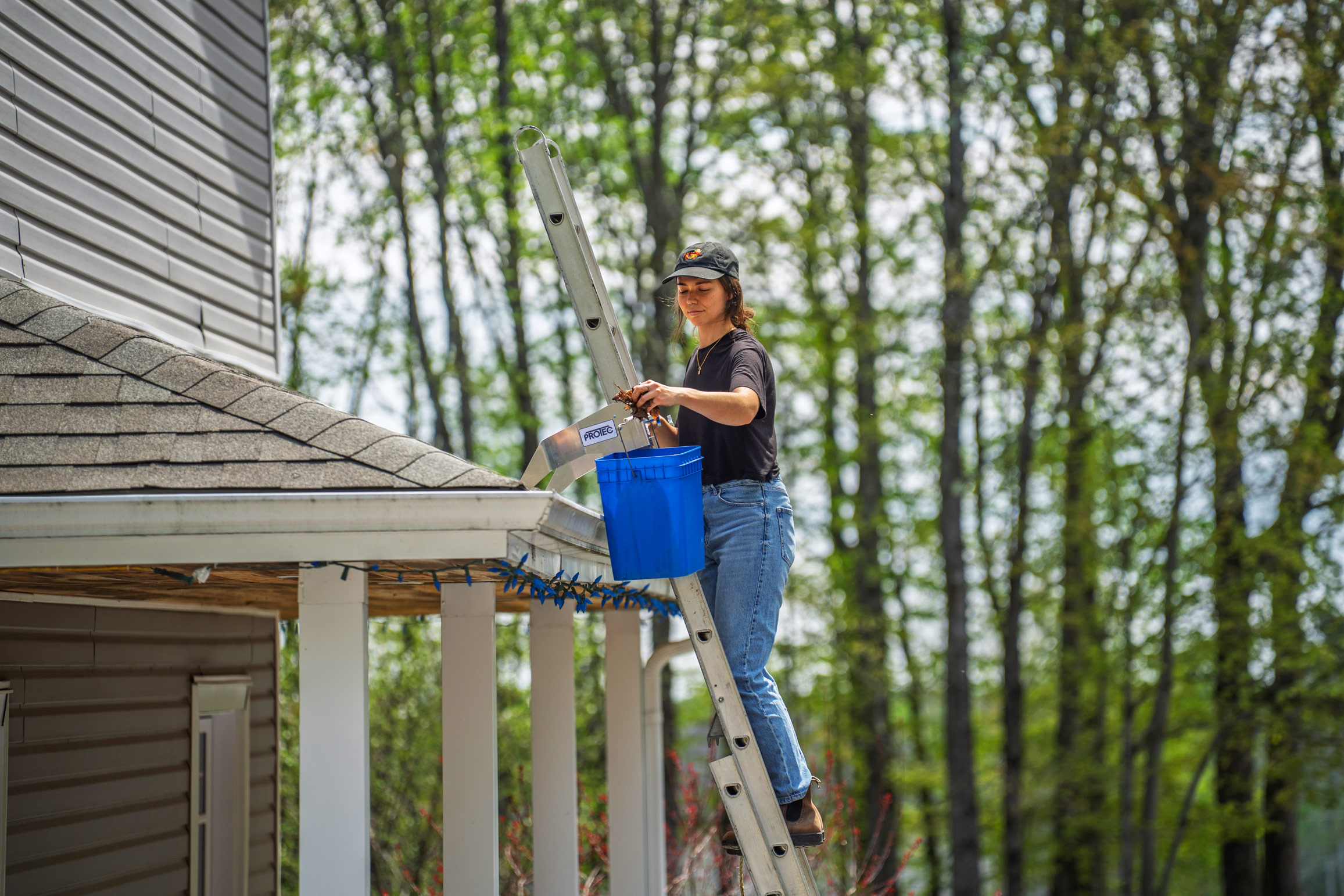 Worker cleaning a gutter from an extension ladder fitted with ProtecMi stabilizers