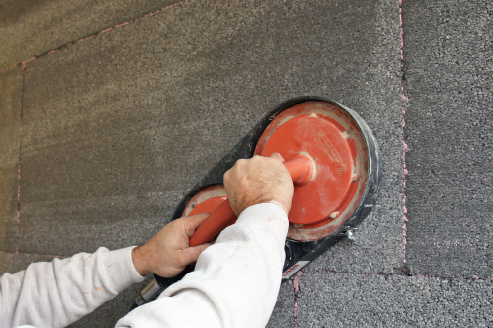 Worker sanding a dark exterior insulation panel with a ROKAMAT Chameleon