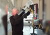 Operator aiming the RigCraftor Pneumatic Strap Launcher beside a flatbed trailer