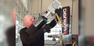 Operator aiming the RigCraftor Pneumatic Strap Launcher beside a flatbed trailer