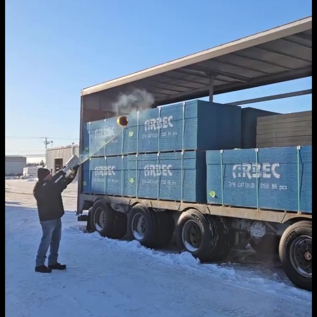 Tie-down strap flying over a tall flatbed truckload after being launched with compressed air