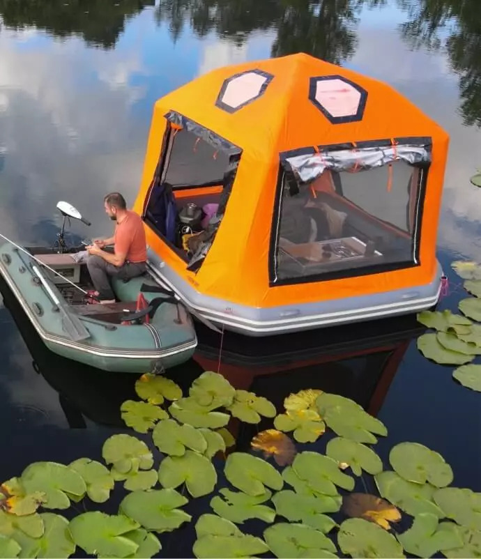 Two people beside the Sönmez Floating Tent in a small boat among water lilies