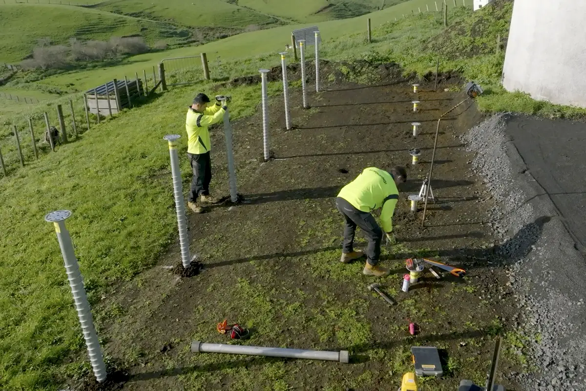 Workers aligning rows of galvanized ground screws on a sloping building site