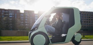 Green HOPPER weather-protected electric cargo bike traveling on a city street