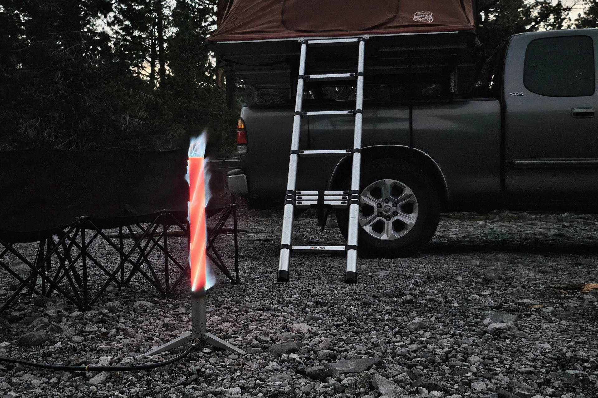 Happy Caveman Campfire glowing beside a pickup truck fitted with a rooftop tent at a campsite