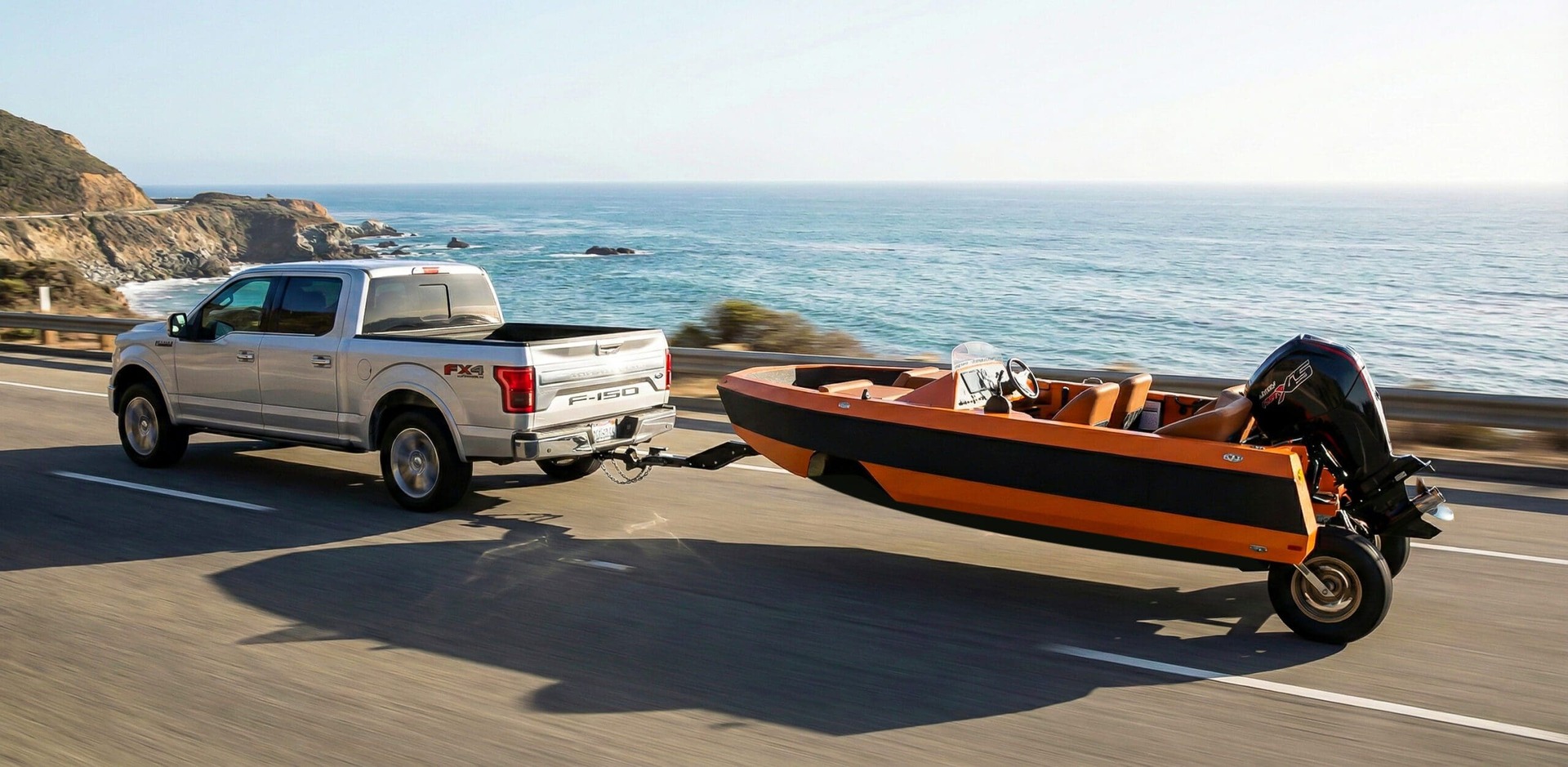 Orange WaterCar EV being towed behind a pickup truck on a coastal highway