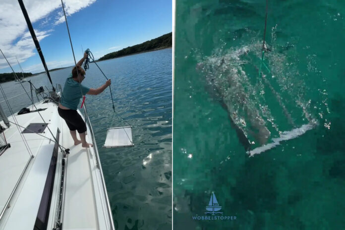 Wobbelstopper mechanical boat stabilizer being lowered beside a sailboat with the flap assembly shown underwater